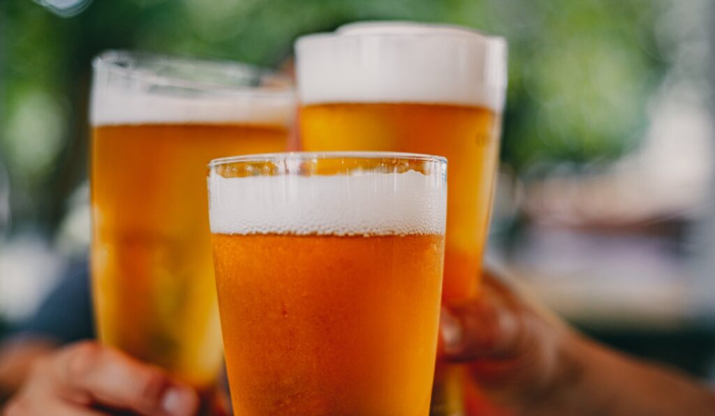 Close-up view of a three glass of beer in hand. Beer glasses clinking at outdoor bar or pub