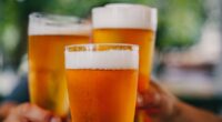 Close-up view of a three glass of beer in hand. Beer glasses clinking at outdoor bar or pub
