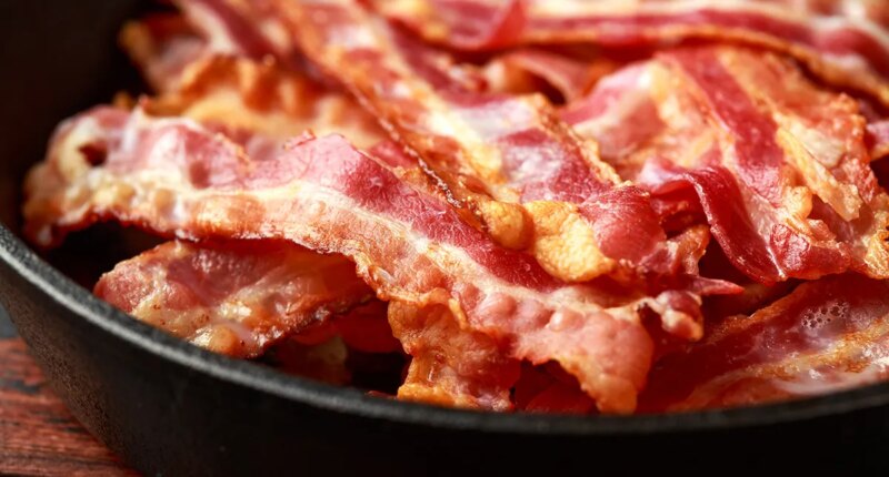 Fried crunchy Streaky Bacon pieces in a cast iron skillet