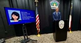 Austin police official stands at podium next to TV screen showing arrested suspect's mugshot