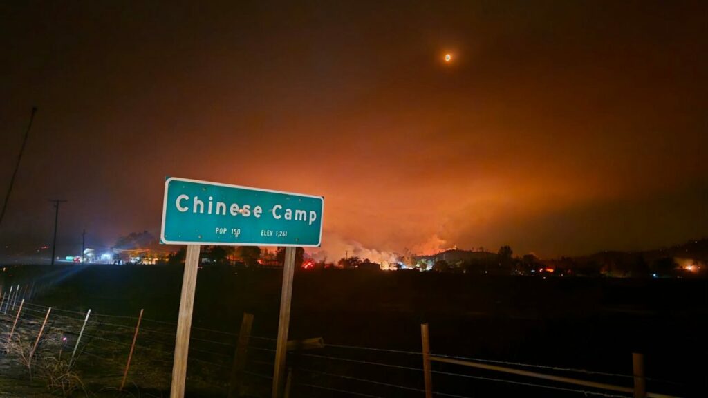A fire blazes behind a sign reading "Chinese Camp."