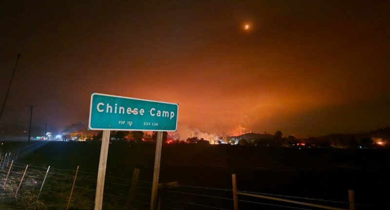 A fire blazes behind a sign reading "Chinese Camp."