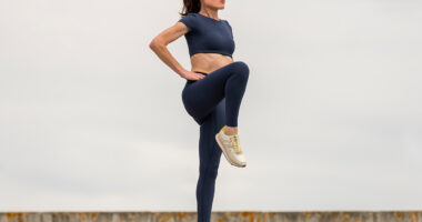 Sporty woman stretching leg muscles with standing single knee to chest stretch, knee drive