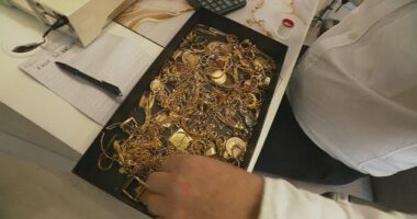 A box full of gold jewellery in a box on a white desk.