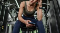 A dedicated young woman seated in the gym, deeply focused on her phone, showcasing the blend of concentration and relaxation during workout routines.