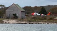 A U.S. Coast Guard helicopter approaches Naushon Island, Mass. Wednesday, Oct. 22, 2025, where a couple and their adult son were rescued two days after their boat caught fire and they swam to shore. (U.S. Coast Guard via AP)