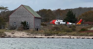 A U.S. Coast Guard helicopter approaches Naushon Island, Mass. Wednesday, Oct. 22, 2025, where a couple and their adult son were rescued two days after their boat caught fire and they swam to shore. (U.S. Coast Guard via AP)