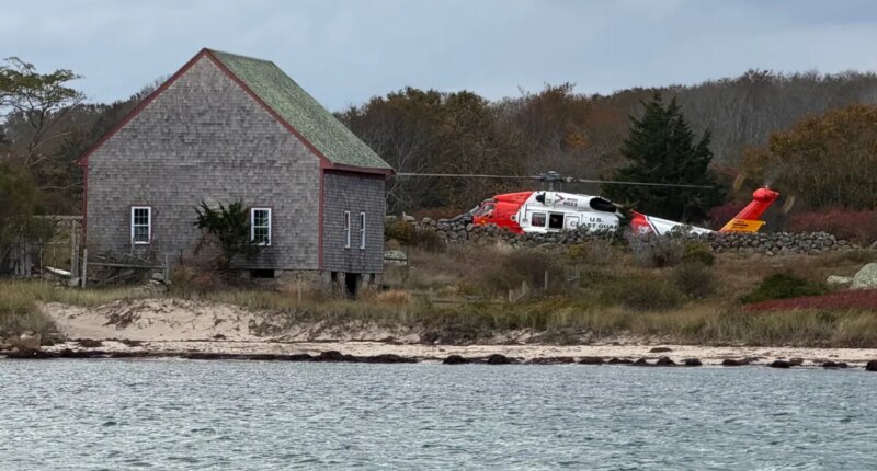 A U.S. Coast Guard helicopter approaches Naushon Island, Mass. Wednesday, Oct. 22, 2025, where a couple and their adult son were rescued two days after their boat caught fire and they swam to shore. (U.S. Coast Guard via AP)