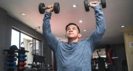 man doing dumbbell overhead presses, exercises to get rid of a dad belly