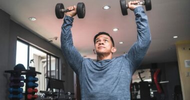 man doing dumbbell overhead presses, exercises to get rid of a dad belly