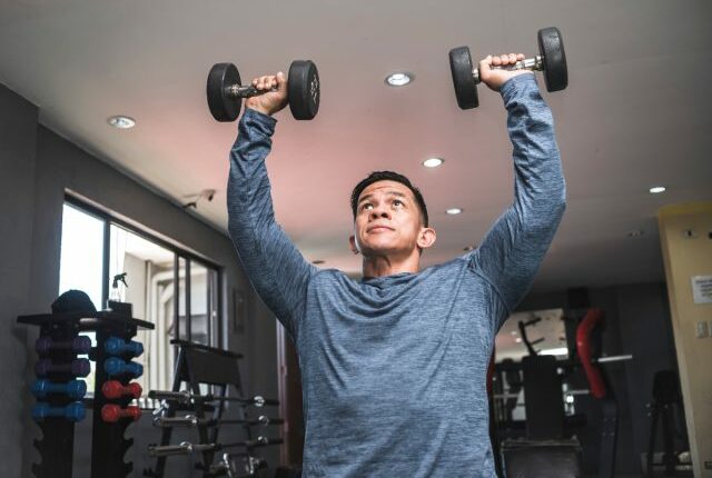 man doing dumbbell overhead presses, exercises to get rid of a dad belly