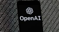 The OpenAI logo appears on a mobile phone in front of a computer screen with random binary data, March 9, 2023, in Boston. (AP Photo/Michael Dwyer, File)