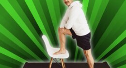 Senior man using a chair to do stretch exercises in a home gym in an effort to keep fit during the Covid-19 pandemic turning to smile at the camera