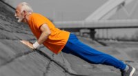 Profile view of an old athlete doing pushups and strength exercises on river shore.