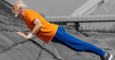 Profile view of an old athlete doing pushups and strength exercises on river shore.