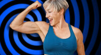 A fit, mature woman with short grey hair flexes her muscles against a pink isolated background, displaying strength and vitality.