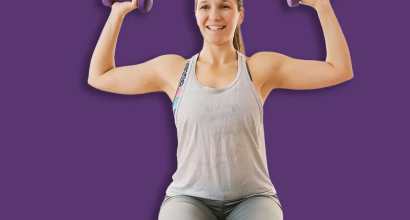Smiling sportswoman sitting on the chair in her apartment and doing exercises for biceps.