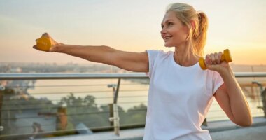 woman outdoors doing arm exercises with dumbbells for lean arms