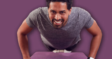 Man In Fitness Clothing At Home In Lounge Doing Press Ups And Exercising With Hand Weights