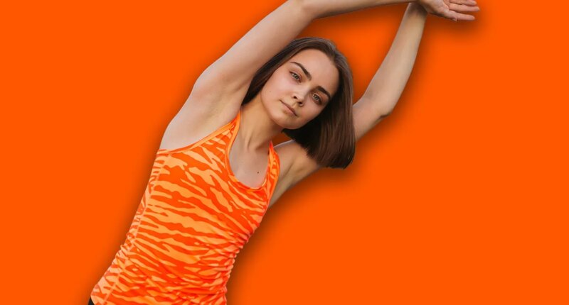 Fit woman in sportswear doing side bend and stretching arms while doing exercise doing fitness workout in summer field and looking at camera