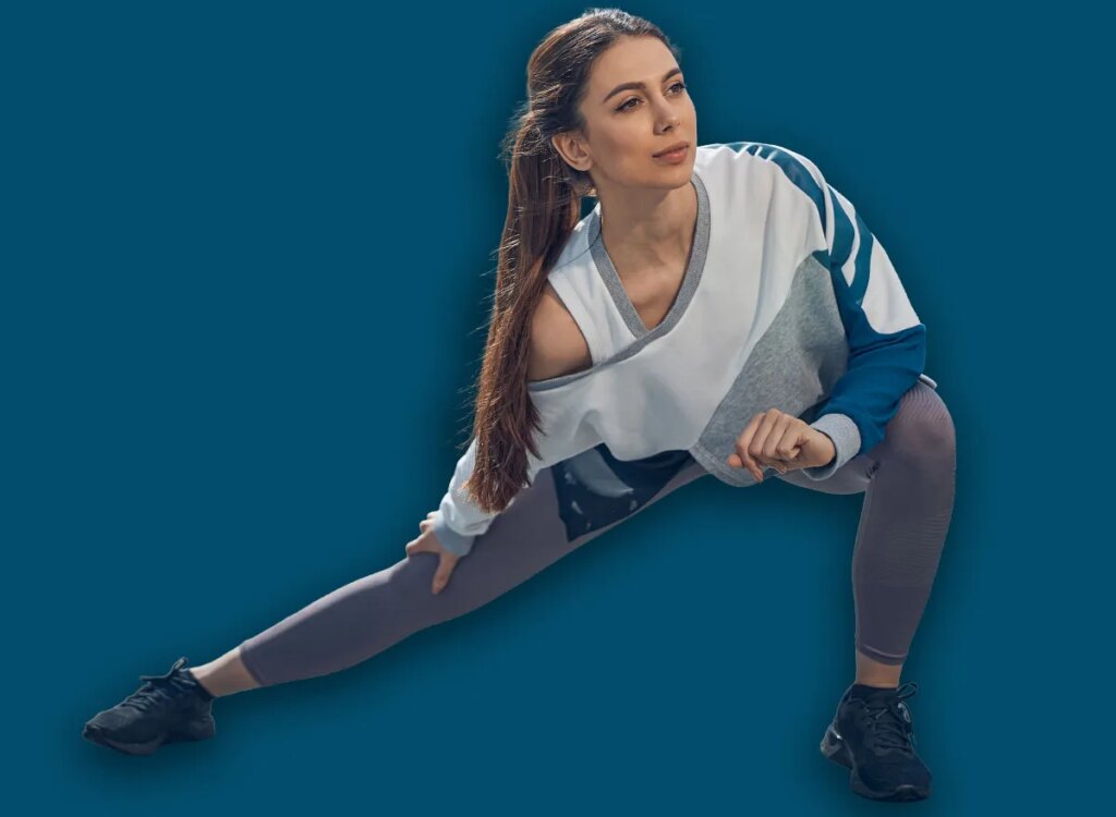 Front view of a young sporty woman with long dark hair doing a side lunge