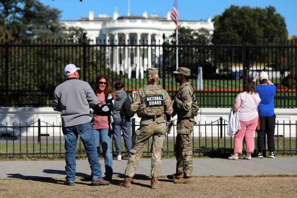 FILE - People talk with National Guard soldiers on the Ellipse, with the White House in the background, Oct. 17, 2025, in Washington. (AP Photo/Rahmat Gul, File)