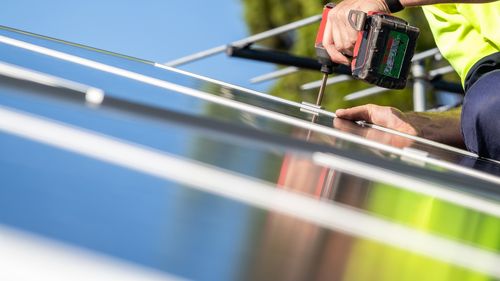 Unidentified electrician performing installation of solar panel on house roof using cordless screwdriver