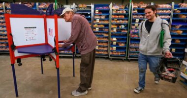 Bob Walser votes while a shopper walks past at the Checkers grocery store in Lawrence, Kan., Tuesday, Nov. 4, 2025. (AP Photo/Charlie Riedel)