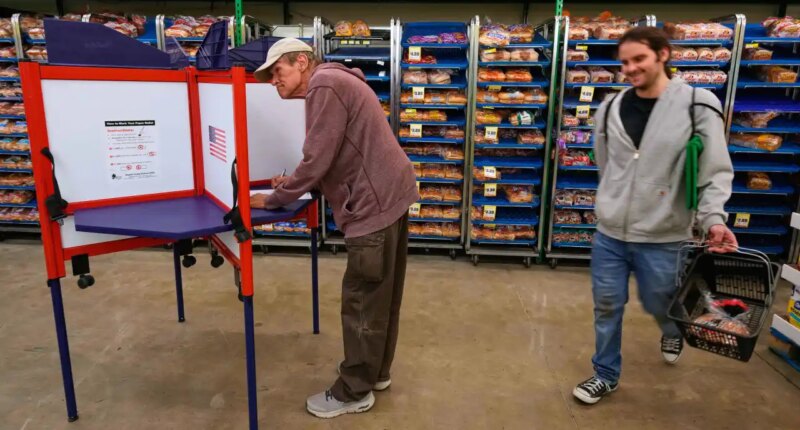 Bob Walser votes while a shopper walks past at the Checkers grocery store in Lawrence, Kan., Tuesday, Nov. 4, 2025. (AP Photo/Charlie Riedel)