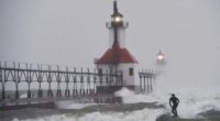 A surfer rides through blowing snow as Lake Michigan waves crash into the St. Joseph Inner and Outer Lighthouses Wednesday, Nov. 26, 2025, in St. Joseph, Mich. (Don Campbell/The Herald-Palladium via AP)