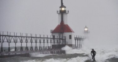 A surfer rides through blowing snow as Lake Michigan waves crash into the St. Joseph Inner and Outer Lighthouses Wednesday, Nov. 26, 2025, in St. Joseph, Mich. (Don Campbell/The Herald-Palladium via AP)