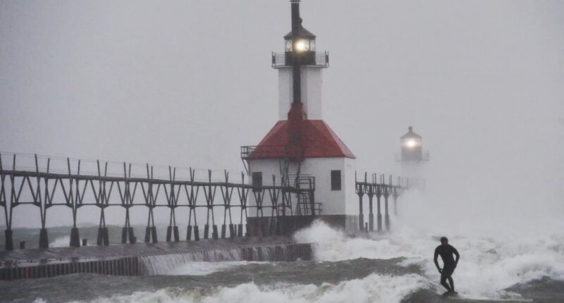 A surfer rides through blowing snow as Lake Michigan waves crash into the St. Joseph Inner and Outer Lighthouses Wednesday, Nov. 26, 2025, in St. Joseph, Mich. (Don Campbell/The Herald-Palladium via AP)