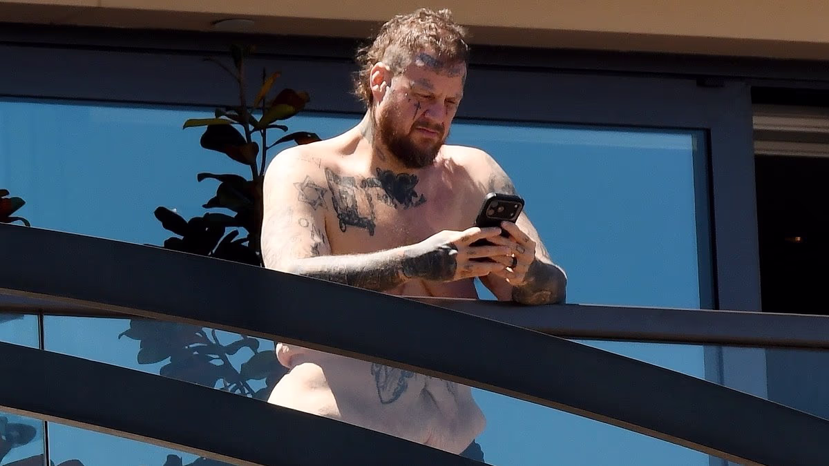Shirtless Jelly Roll is seen enjoying the sun on his hotel balcony in Sydney as he is slammed for cancelling his Auckland concert one hour before he was due on stage