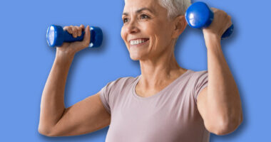 Active European senior lady with stylish haircut stays fit exercising with dumbbells, lifting weight flexing arms muscles, standing at home indoor. Domestic workout concept