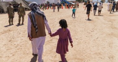 FILE - A man walks with a child through Fort Bliss