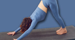 Beautiful yogi woman working out indoors, doing yoga exercise in room on mat, downward facing dog pose, adho mukha svanasana, sun salutation pose, sport fitness exercise for wellness, weight loss