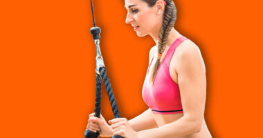 Happy and beautiful fit woman wearing pink fitness bra while exercising cable rope triceps extension at the gym
