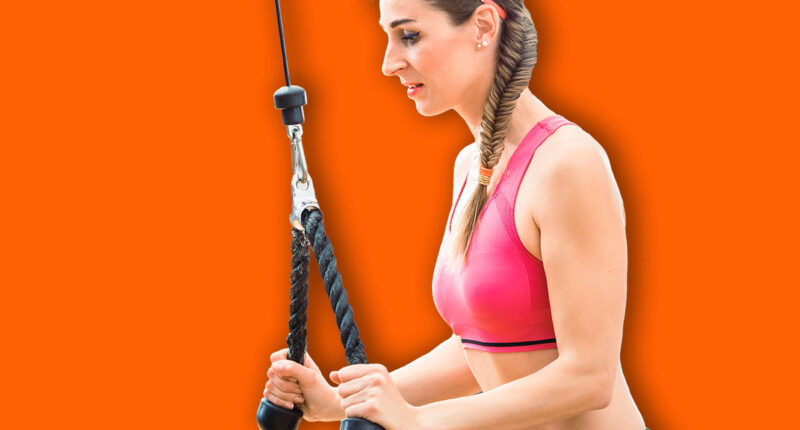 Happy and beautiful fit woman wearing pink fitness bra while exercising cable rope triceps extension at the gym