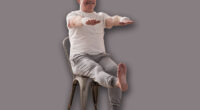 Elderly man practicing yoga asana or sport exercise for legs and hands on chair