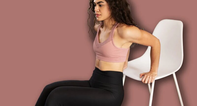 Athletic latin woman in her 20s working out her arms with tricep dips exercises. Good-looking woman using a chair for her home workout