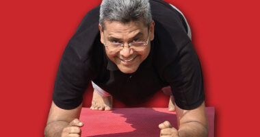 Senior Indian man doing forearm plank on a yoga mat outdoors, smiling and enjoying his fitness routine in the fresh morning air at Riverfront, Ahmedabad. Man is staying fit after 60 years of age.