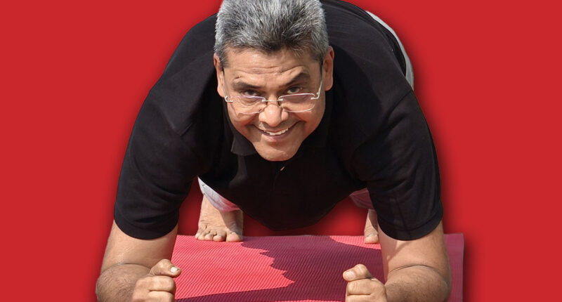 Senior Indian man doing forearm plank on a yoga mat outdoors, smiling and enjoying his fitness routine in the fresh morning air at Riverfront, Ahmedabad. Man is staying fit after 60 years of age.