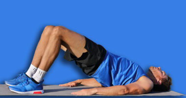 Fitness man doing bodyweight glute floor bridge pose yoga exercise. Fit athlete exercising glutes muscles with butt raise at summer outdoor gym instruction class on grass.
