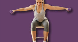 Smiling muscular woman in shape sitting on the chair at home and doing fitness exercises for arms with dumbbells.