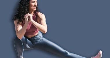 Young smiling fit woman doing stretching exercises for legs before training. Female athlete preparing for jogging outdoors. Runner doing side lunges. Active lifestyle concept.