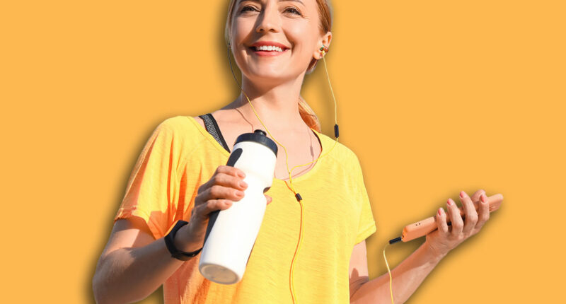 Sporty mature woman with bottle of water listening to music outdoors