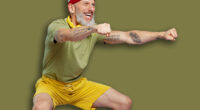 Full size body length fitness vivid elderly gray-haired bearded man 40s years old in headband khaki t-shirt look aside doing side squat isolated on plain pastel light purple background studio portrait
