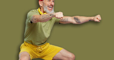 Full size body length fitness vivid elderly gray-haired bearded man 40s years old in headband khaki t-shirt look aside doing side squat isolated on plain pastel light purple background studio portrait