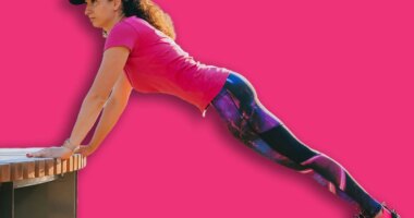 Woman doing incline push-ups on a bench in an outdoor gym, focusing on strength and endurance during her fitness routine in an urban park