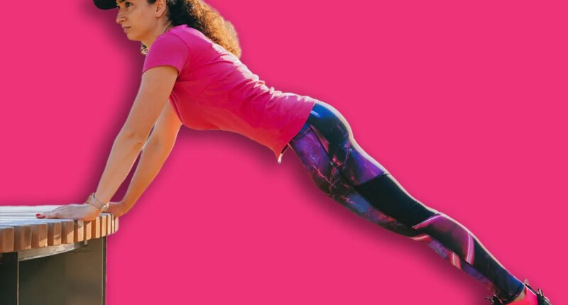 Woman doing incline push-ups on a bench in an outdoor gym, focusing on strength and endurance during her fitness routine in an urban park